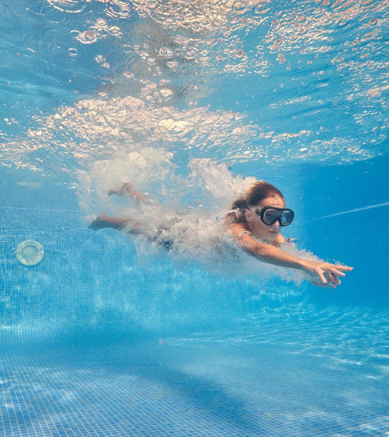 Active boy swimming underwater of clear pool